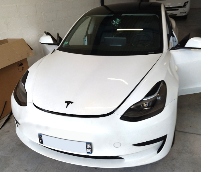 Réparation pare-brise Tesla Model 3 blanche, toit noir, portières ouvertes, vue de face.