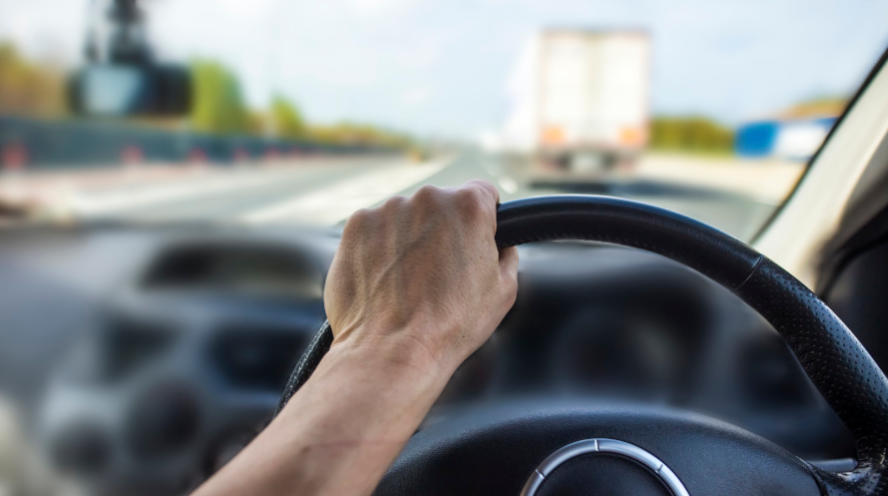 Conduite sécurisée : main sur le volant, pare-brise intact, camion visible au loin.