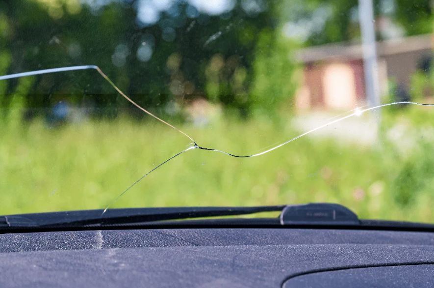 Fissure sur pare-brise d'une voiture en mouvement, illustrant les risques de visibilité réduite et d'accident.